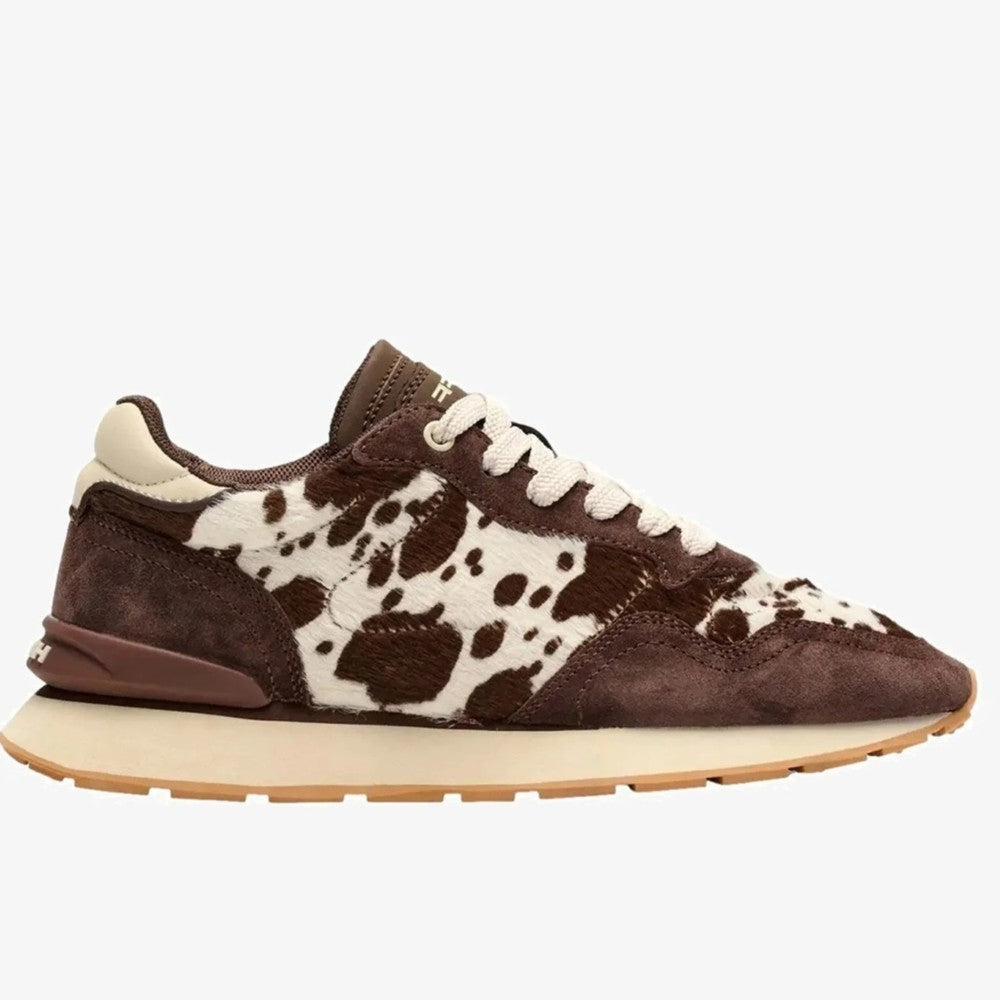 A Hoff low-top sneaker featuring a brown and white cowhide pattern on the upper, brown suede overlays, white laces, and a thick cream midsole with a gum outsole, shown against a plain light grey background.