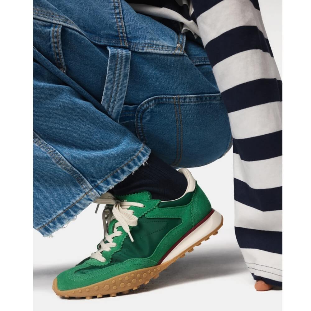 Green sneaker with brown sole worn by a person in blue jeans and a striped shirt. Hoff Bridge MK II Green