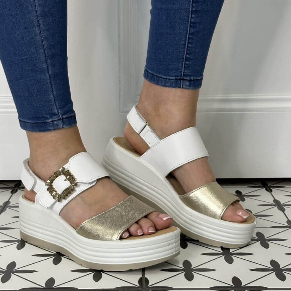 Igi & Co White and gold sandals worn with blue jeans on a patterned floor.