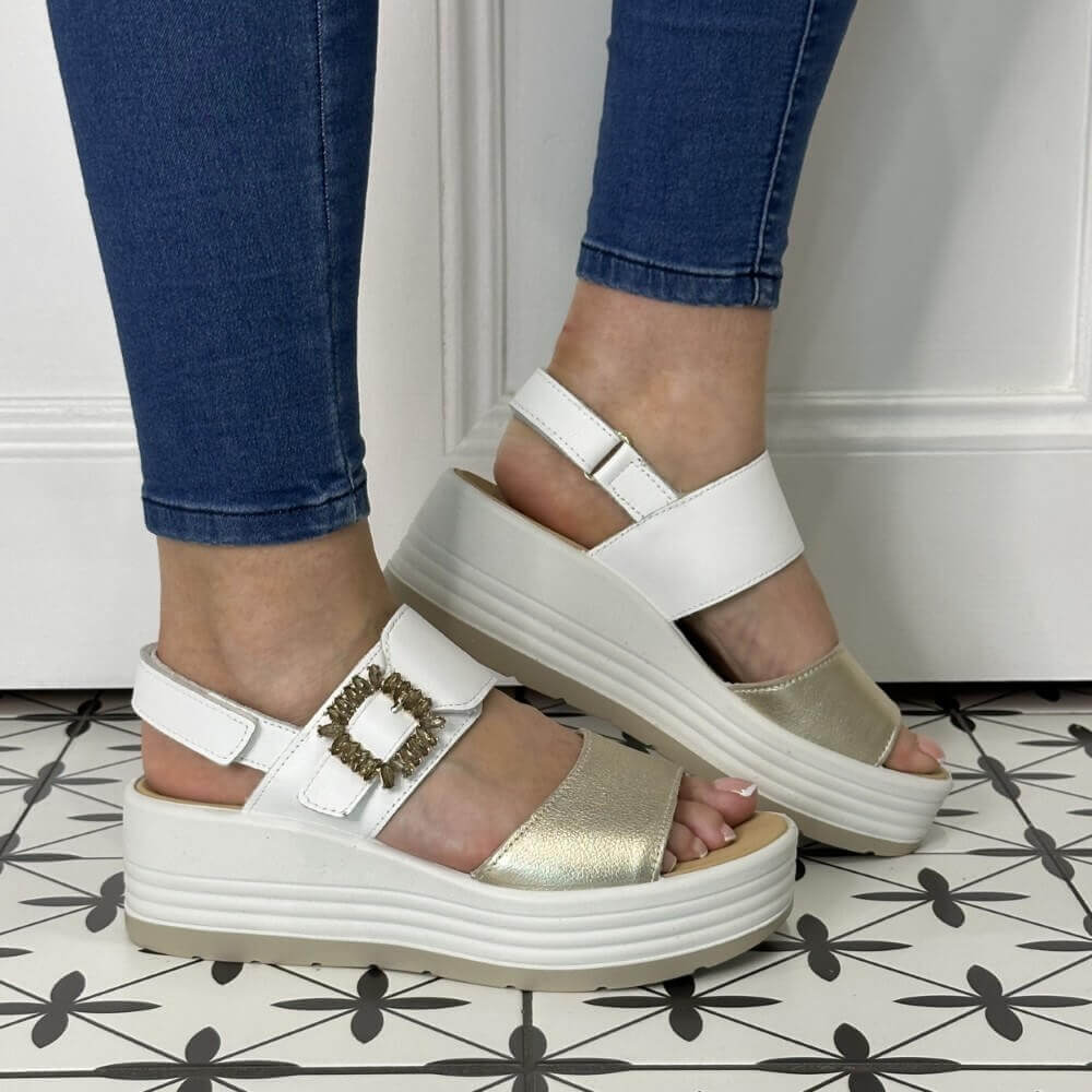 Igi & Co White and gold sandals worn with blue jeans on a patterned floor.