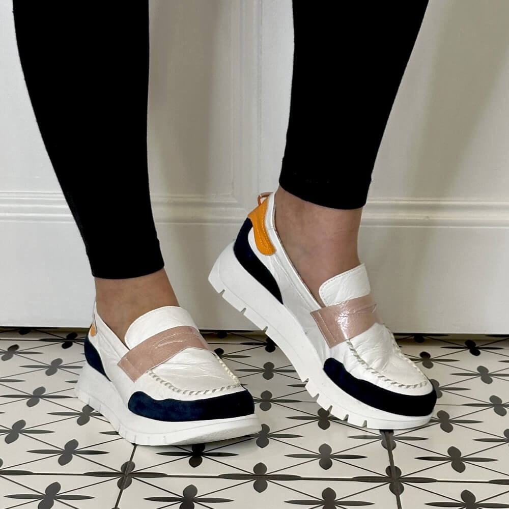 White sneakers with orange and navy accents worn by a person on a tiled floor.