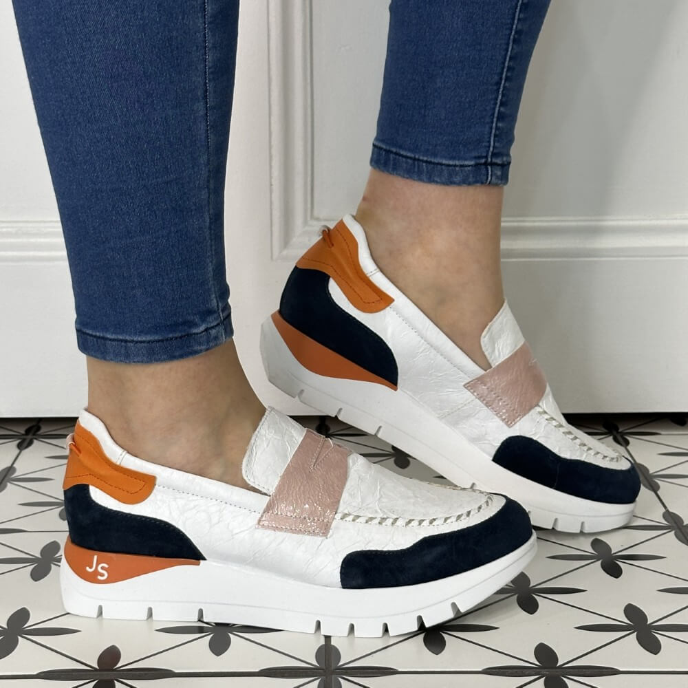 White sneakers with orange and navy accents worn by a person on a tiled floor.