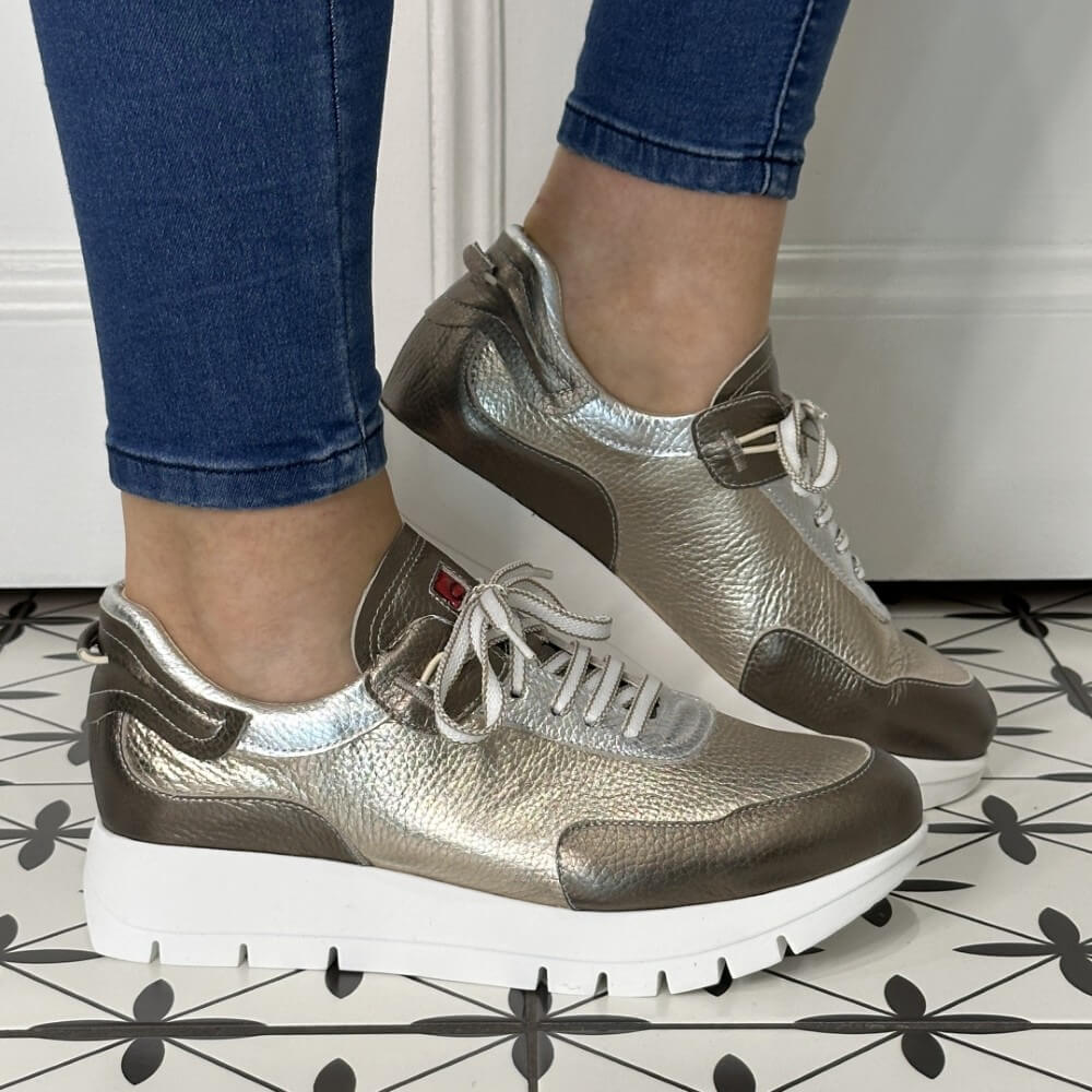 Gold, Silver and brown sneakers worn with blue jeans on a patterned floor.