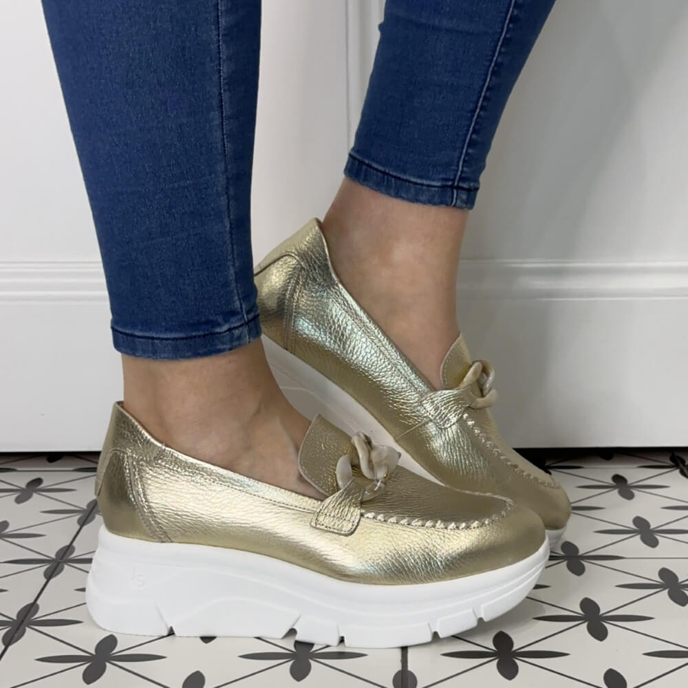 Gold loafers worn with blue jeans on a tiled floor.