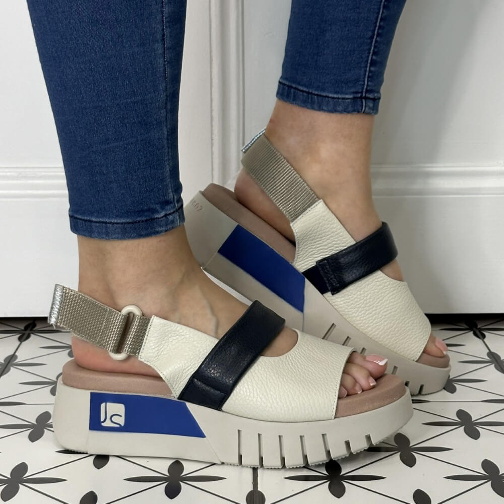 off White sandals with navy and blue straps worn by a person on a tiled floor.
