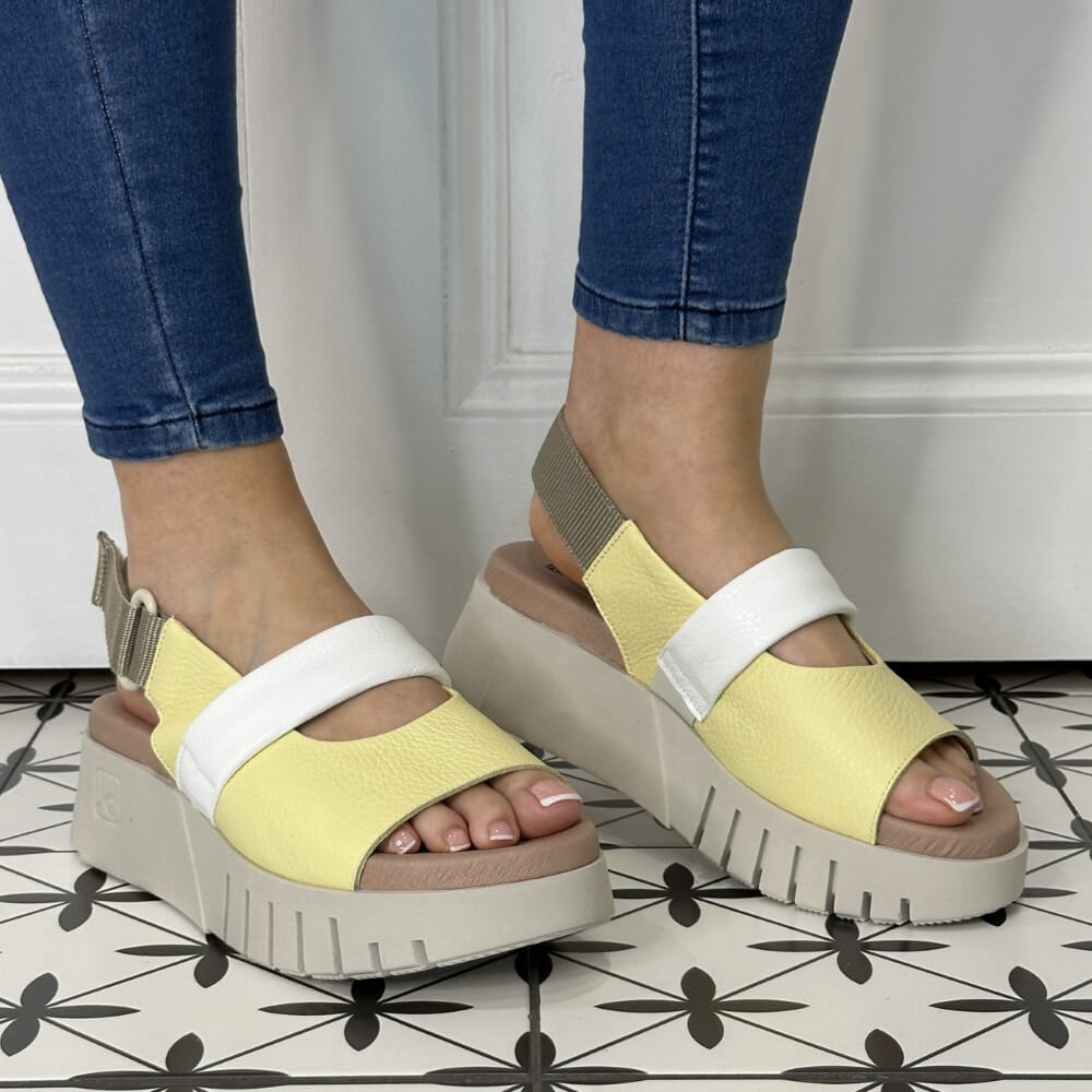 Yellow platform sandals worn with blue jeans on a patterned floor.