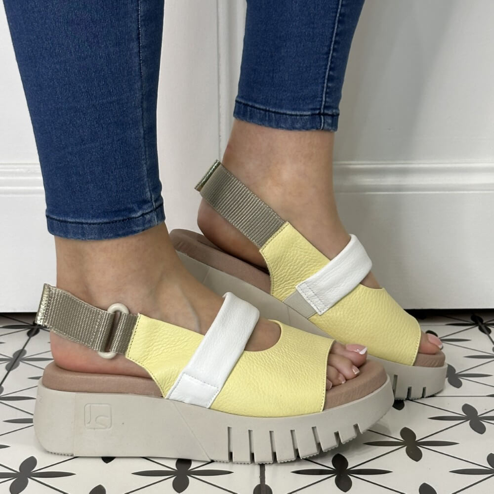 Yellow sandals with white straps worn by a person on a patterned floor.