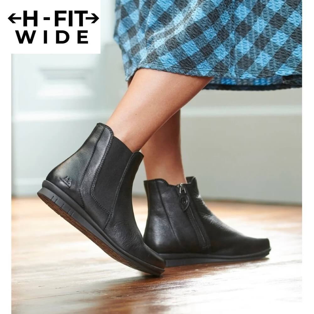 A person wearing Josef Seibel black leather ankle boots with side zippers, shown from the knees down on a wooden floor. The top of the frame includes a white overlay reading 'H-FIT WIDE'.