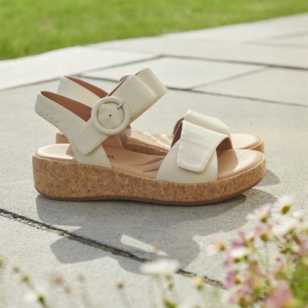 White sandals with cork sole on a concrete surface with grass and flowers in the background