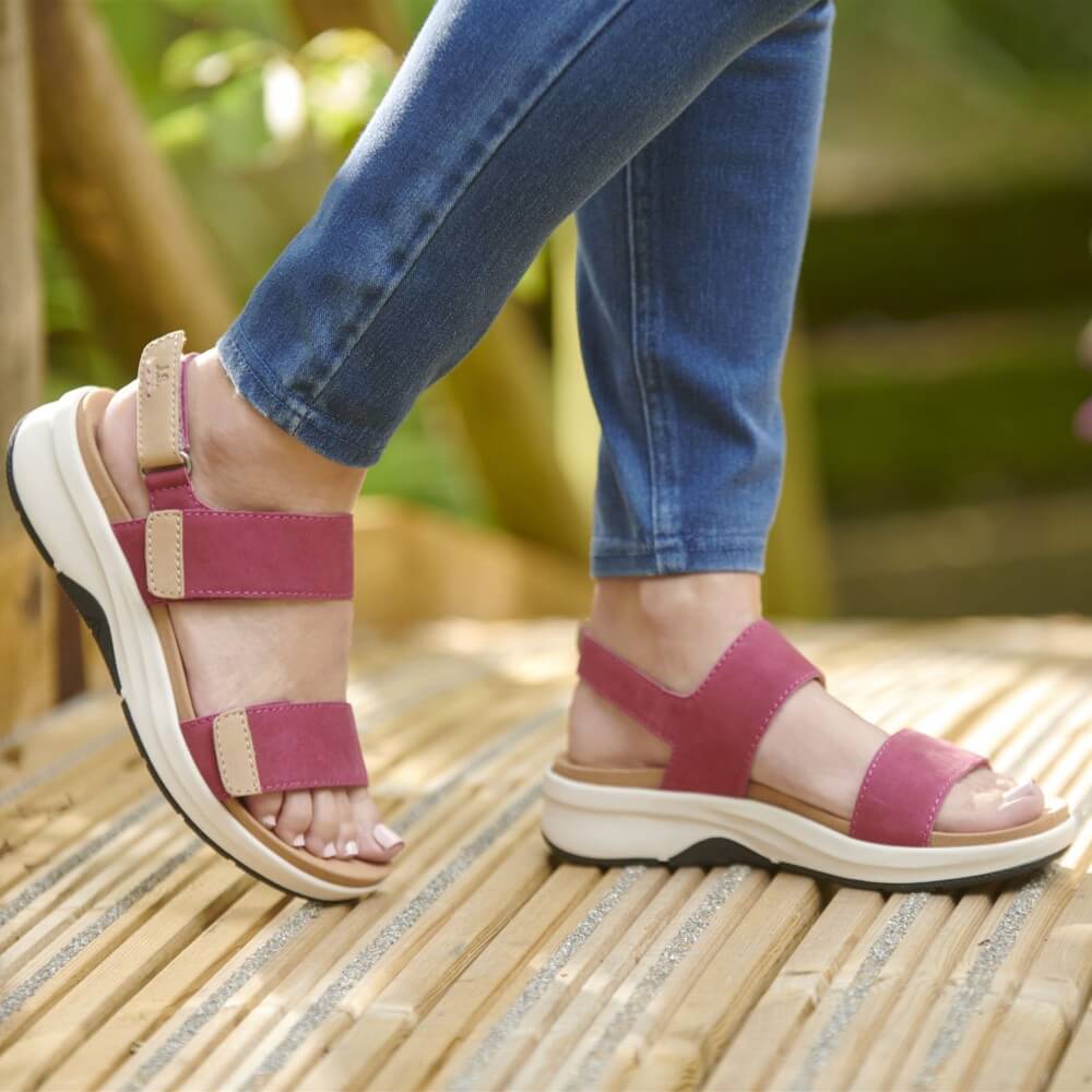 Person wearing Josef Seibel pink sandals with brown straps on a wooden floor.
