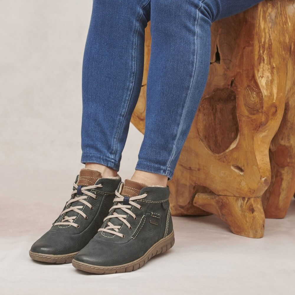 Person wearing green boots with blue jeans standing on a light background