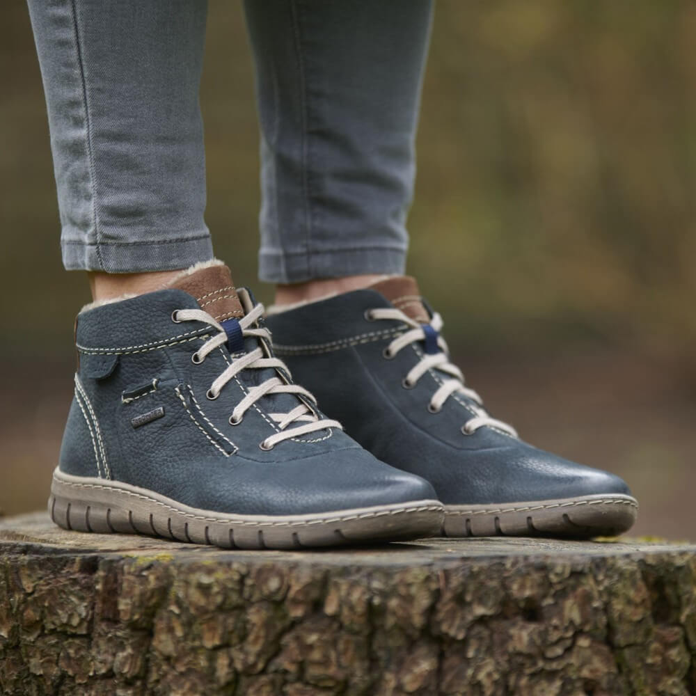 Blue waterproof boots with brown accents worn by a person standing on a wooden stump.