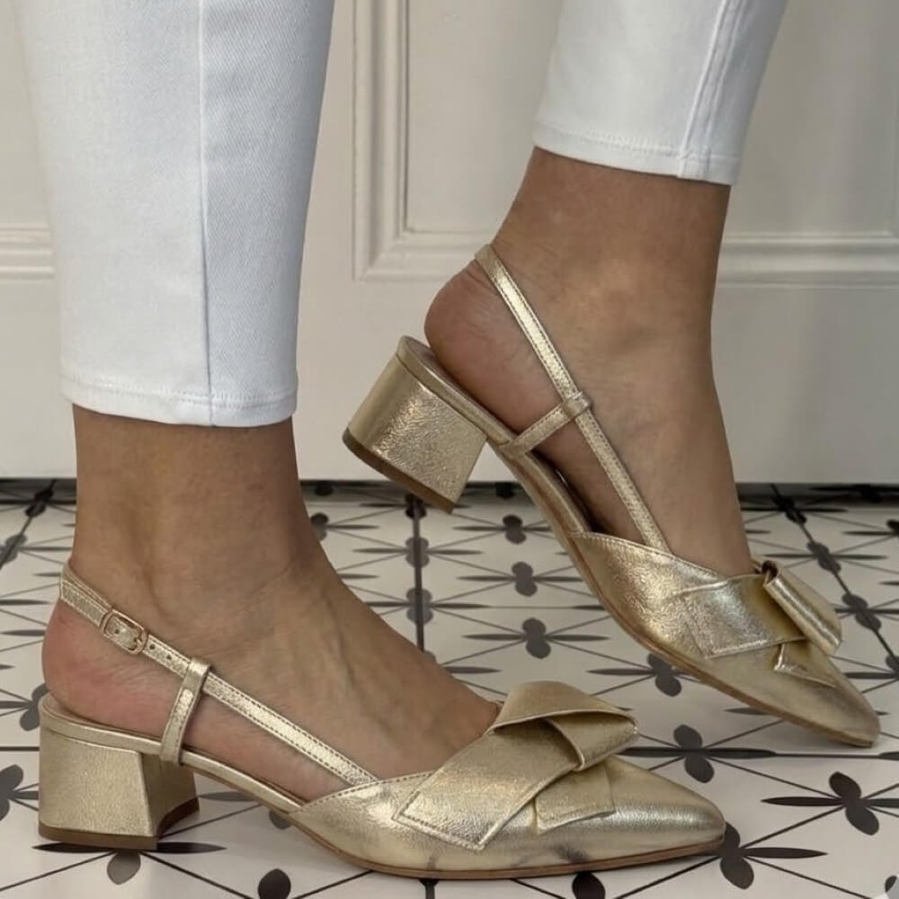 Lodi Gold metallic shoes with bow detail worn by a person on a patterned floor.