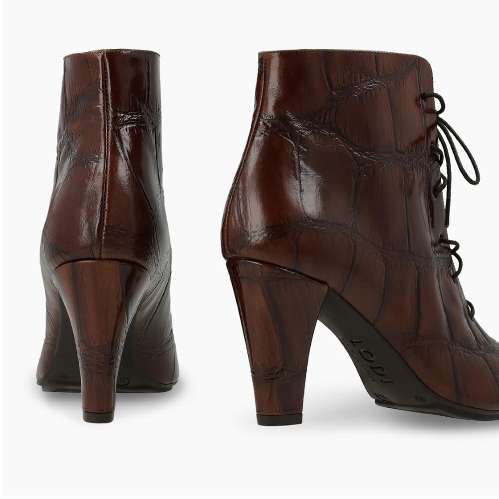A pair of Lodi dark brown ankle boots with a crocodile-embossed texture, featuring a block heel and black laces, shown from the back and side on a white background.