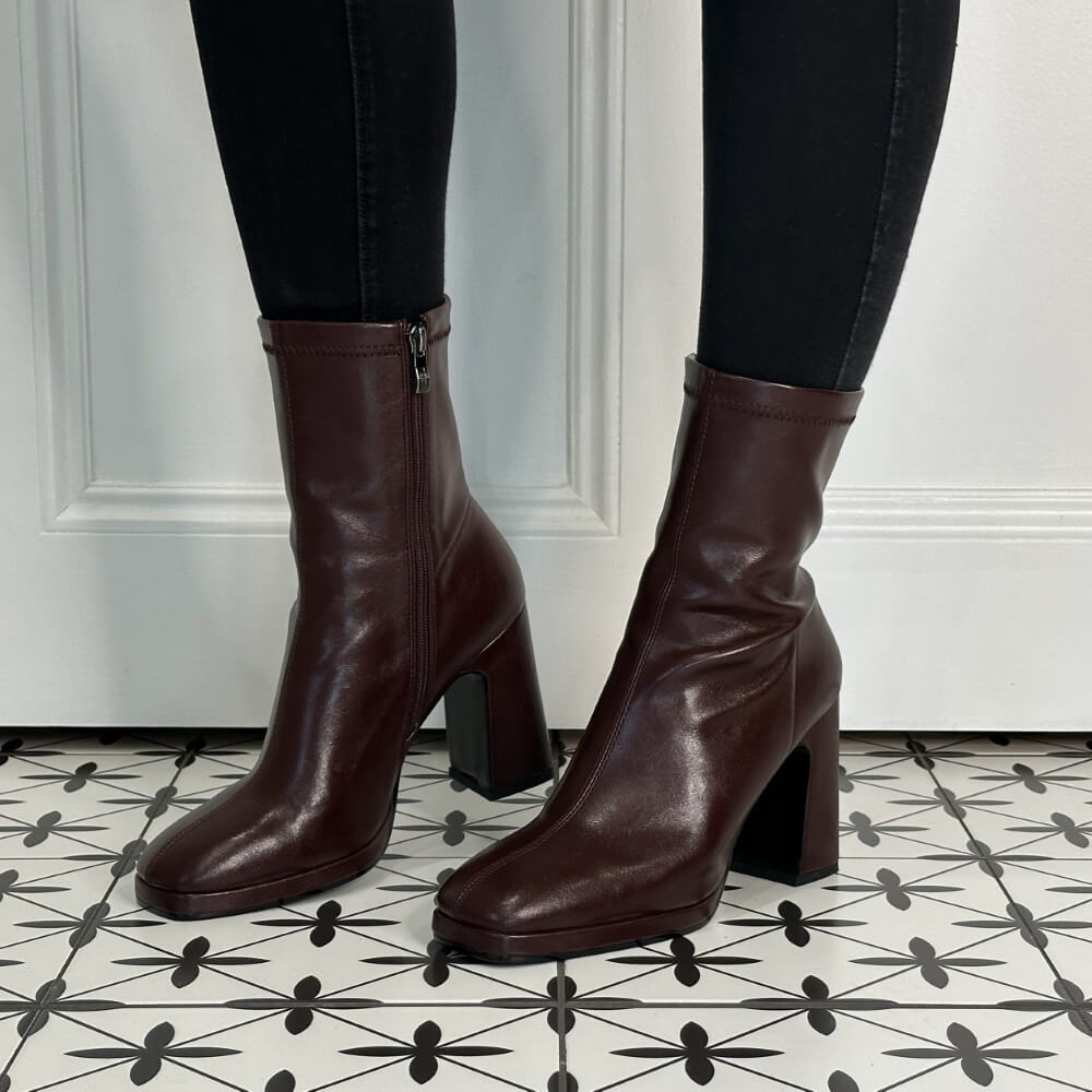 Burgundy boots worn with black pants on a patterned floor.