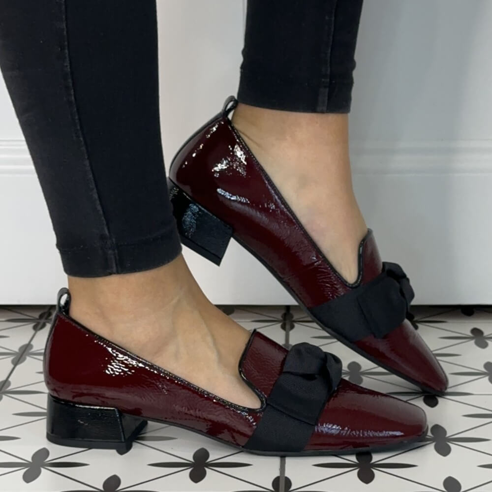 Burgundy shoes with black bows worn indoors on a patterned floor.