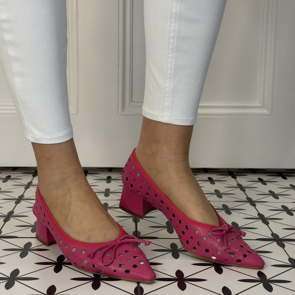 Person wearing pink perforated shoes with a bow on a patterned floor.