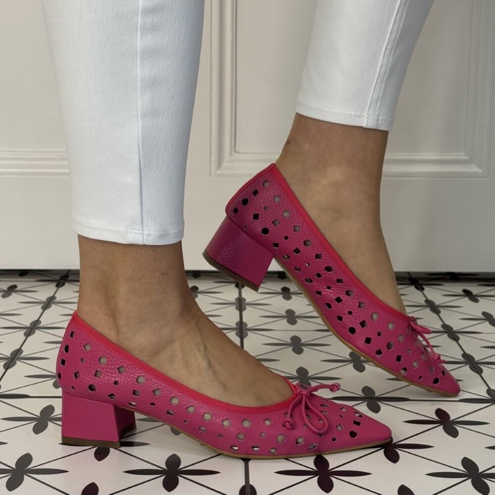 Pink perforated shoes worn with white pants on a patterned floor.