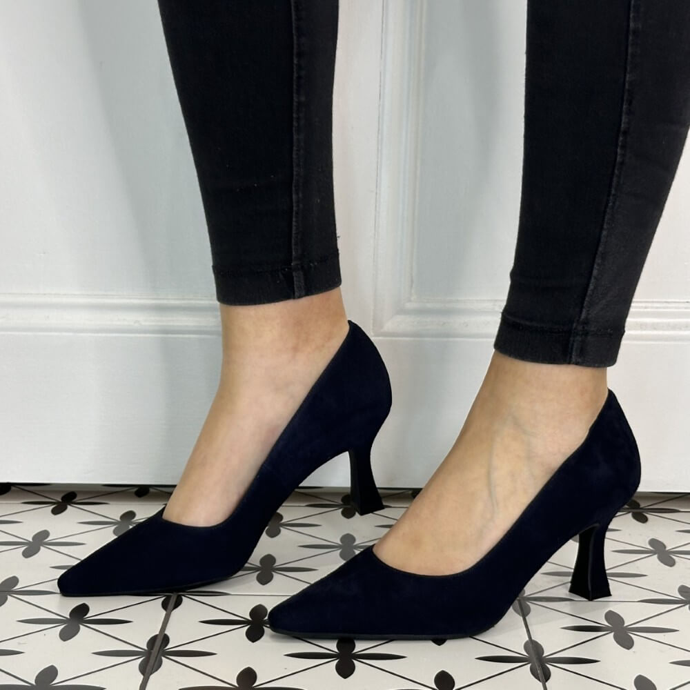 Navy blue high-heeled shoes worn with black pants on a patterned floor.