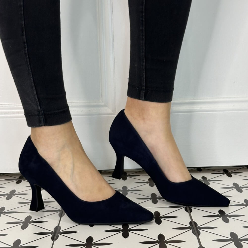 Navy high-heeled shoes worn with black pants on a patterned floor.