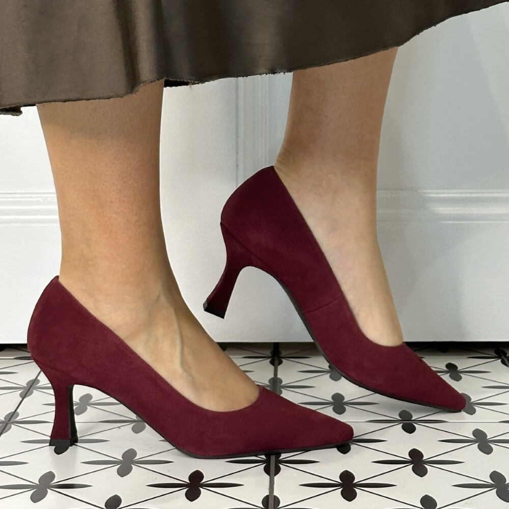 Burgandy suede high-heeled shoes worn by a person on a patterned floor.