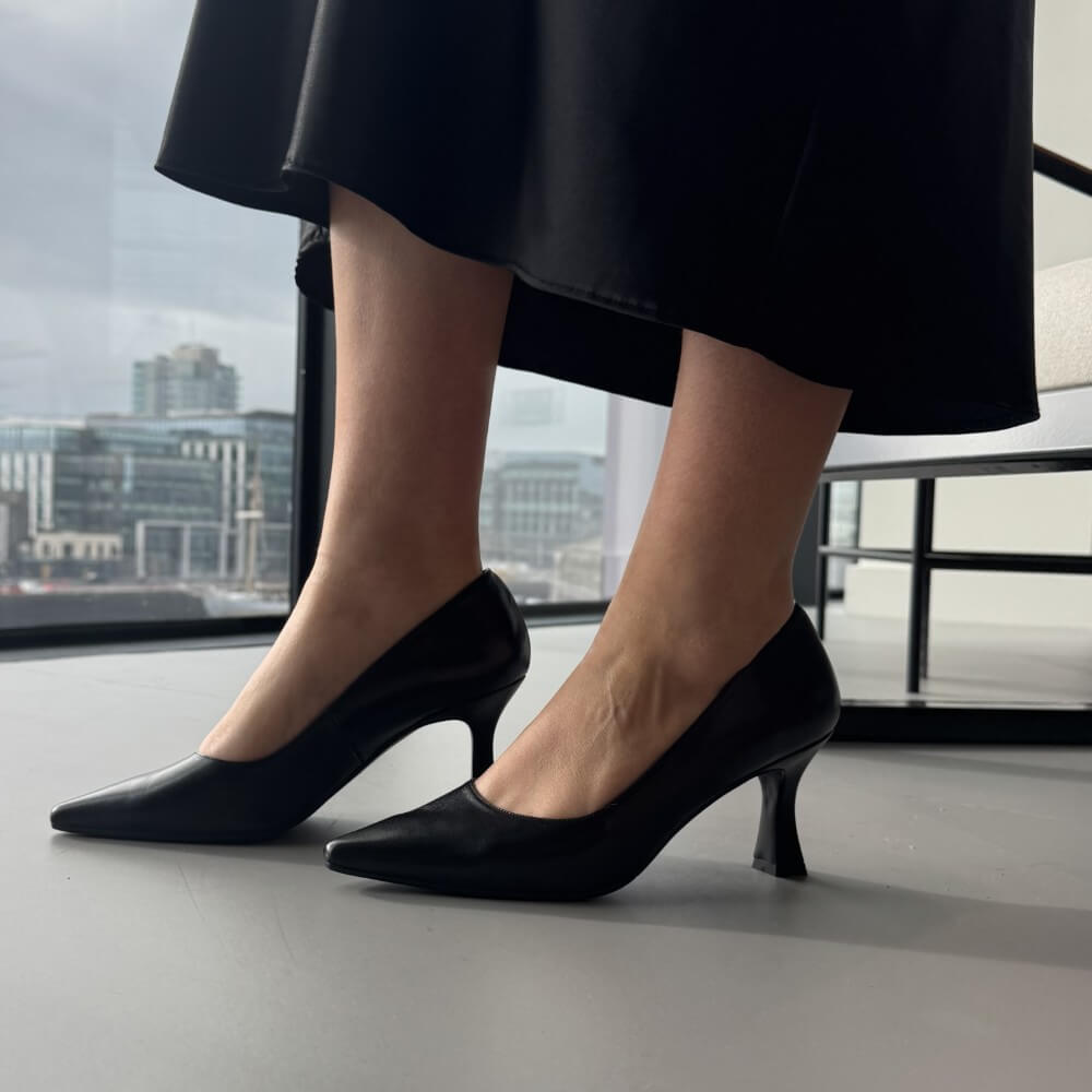 Black high-heeled shoes worn with a black skirt against an urban background