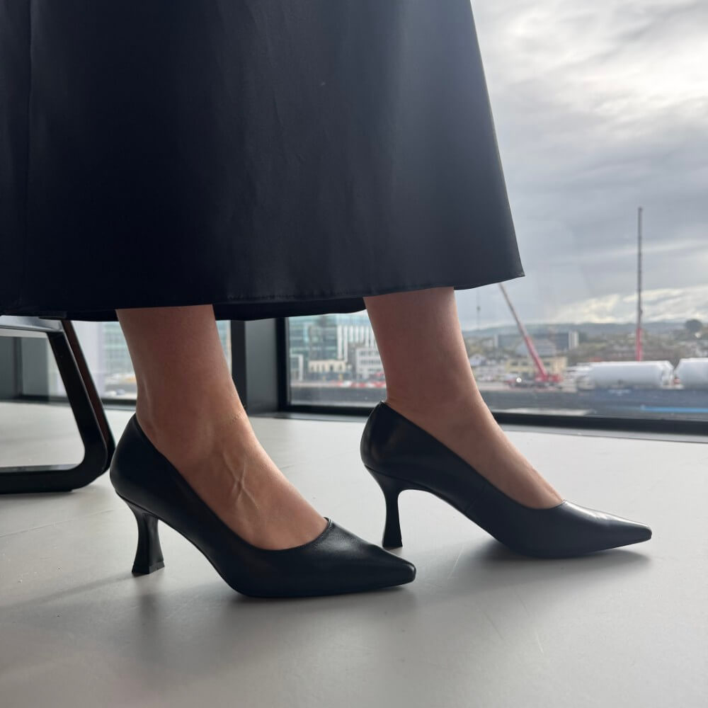 Person wearing black high-heeled shoes and a black skirt in an indoor setting.