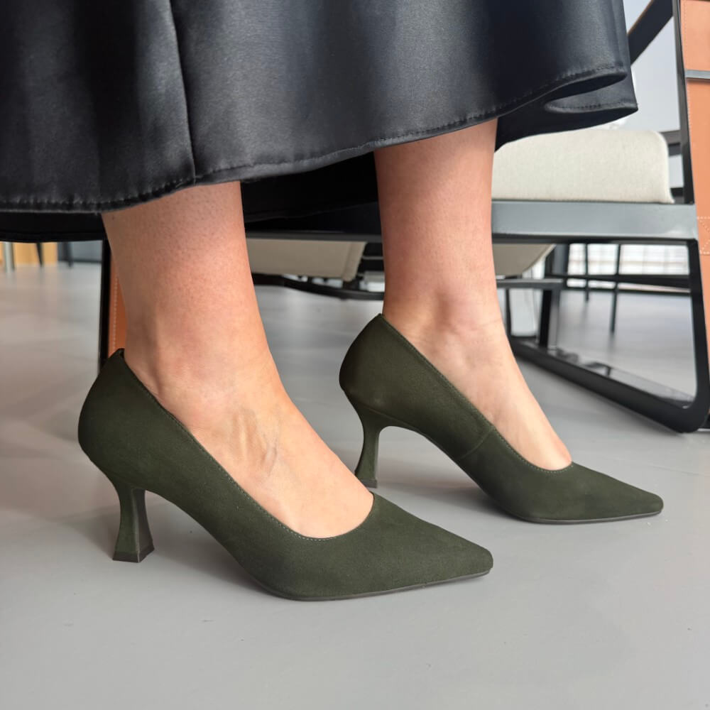 Green high-heeled shoes worn by a person sitting on a chair.