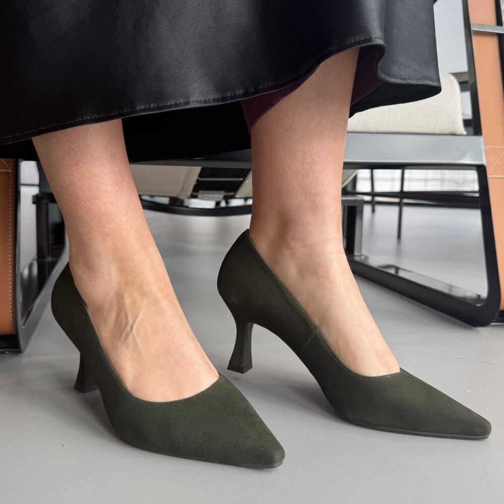 Green high-heeled shoes worn by a person sitting on a chair.