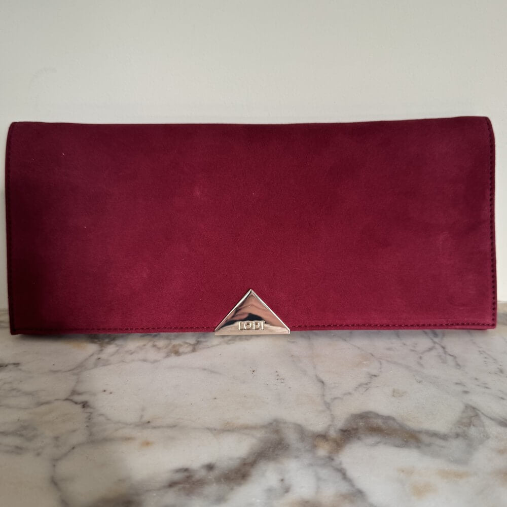 Burgundy Red Clutch with a gold Lodi emblem on a marble surface