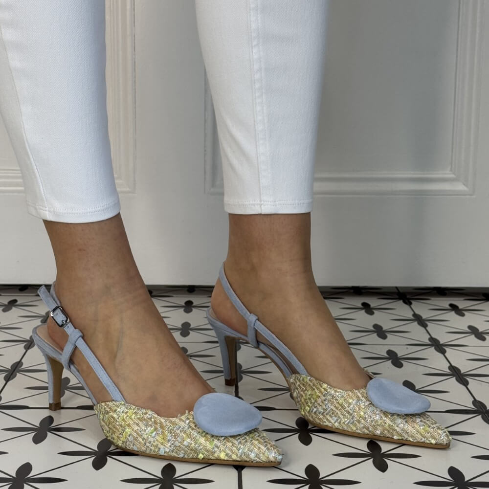 Gold and silver high-heeled shoes with blue accents worn by a person on a patterned floor.