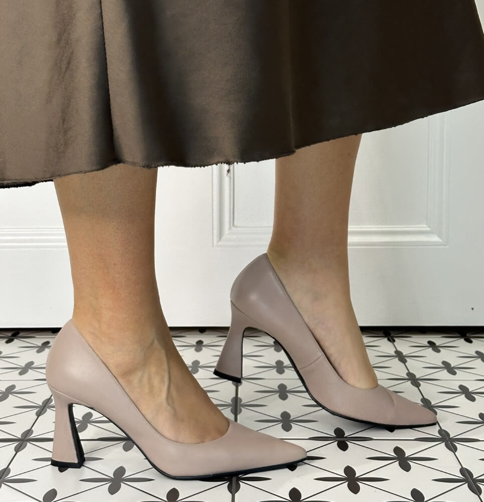 Nude Leather high-heeled shoes worn with a brown skirt on a patterned floor.