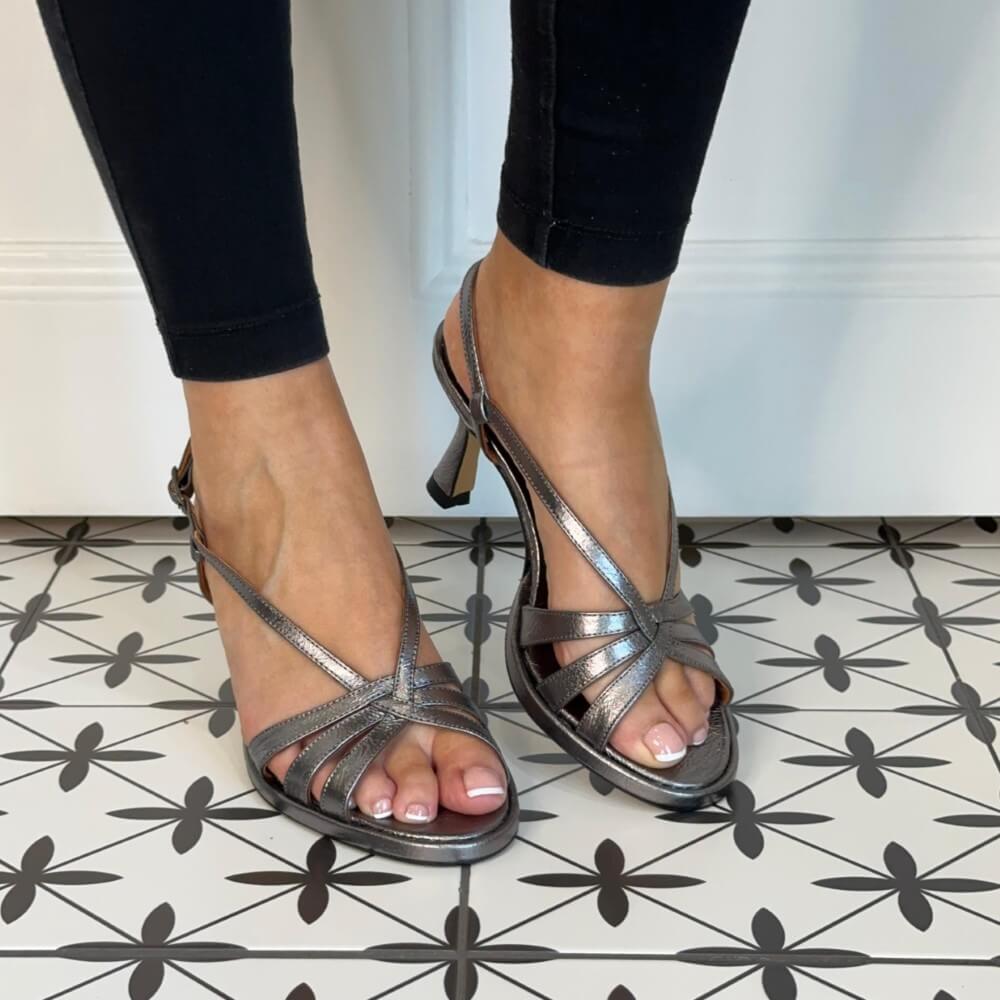 Dark Silver high-heeled sandals worn with black pants on a patterned floor, next to a matching Darksilver handbag. Marian 53305 Slingback Sandal Pewter Metallic