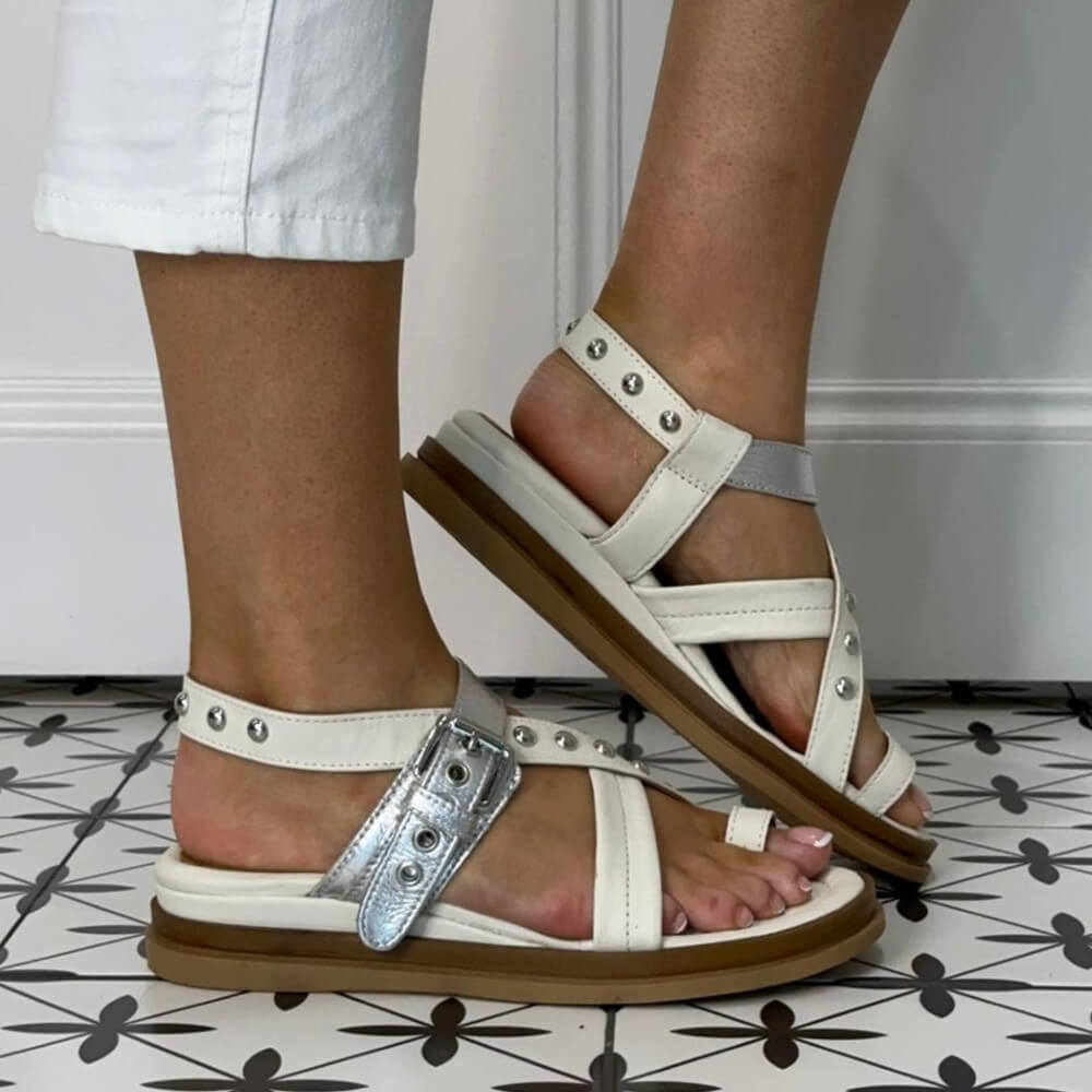 MJUS white and silver sandals with brown soles worn by a person on a patterned floor.