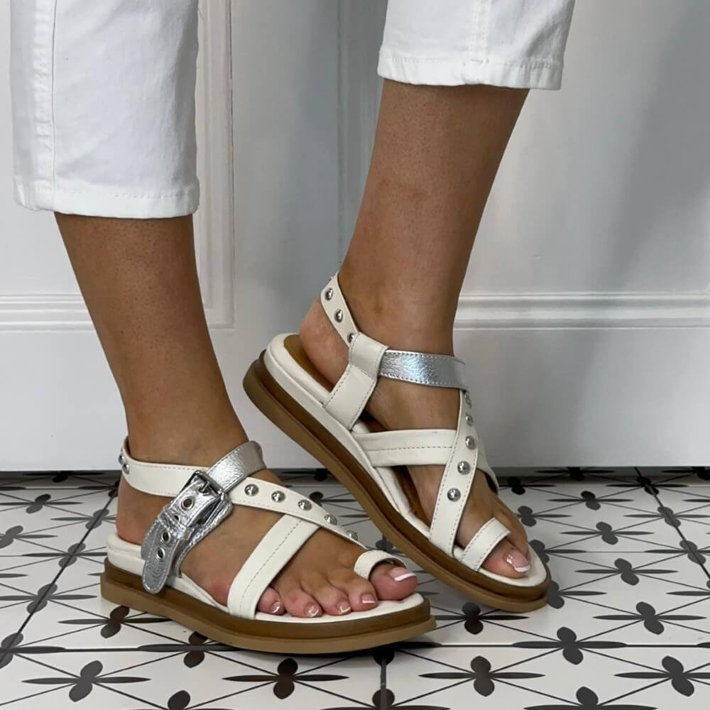 MJUS white and silver sandals with brown soles worn by a person on a patterned floor.