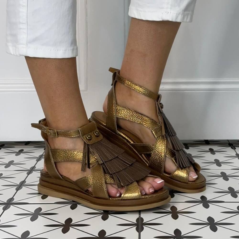 MJUS Gold sandals with fringe details worn by a person on a patterned floor.