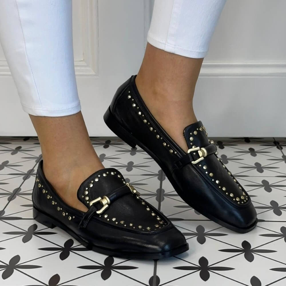MJUS Black loafers with gold accents worn on a patterned floor.