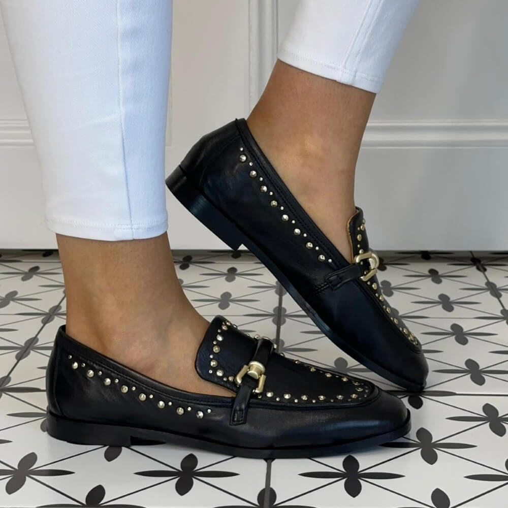 MJUS Black loafers with gold accents worn on a patterned floor.