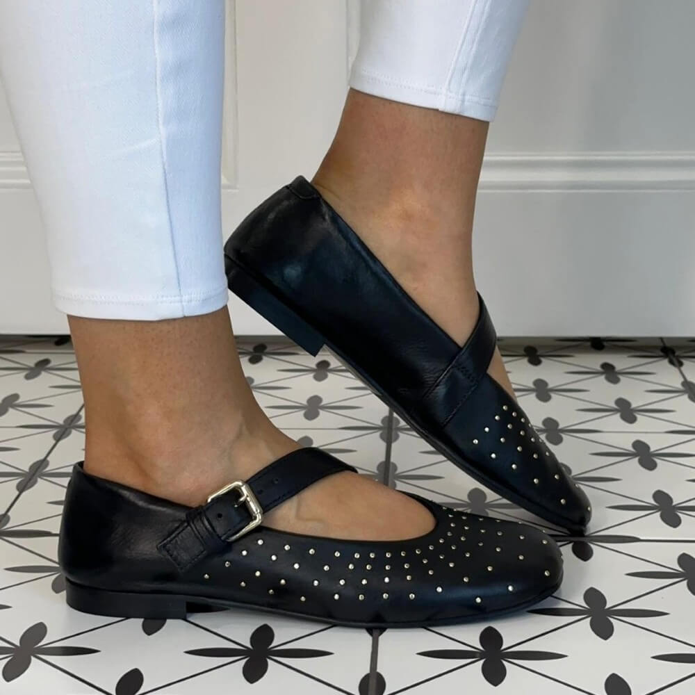 MJUS Black Leather Mary-Jane flat shoes with silver dots worn by a person on a patterned floor.
