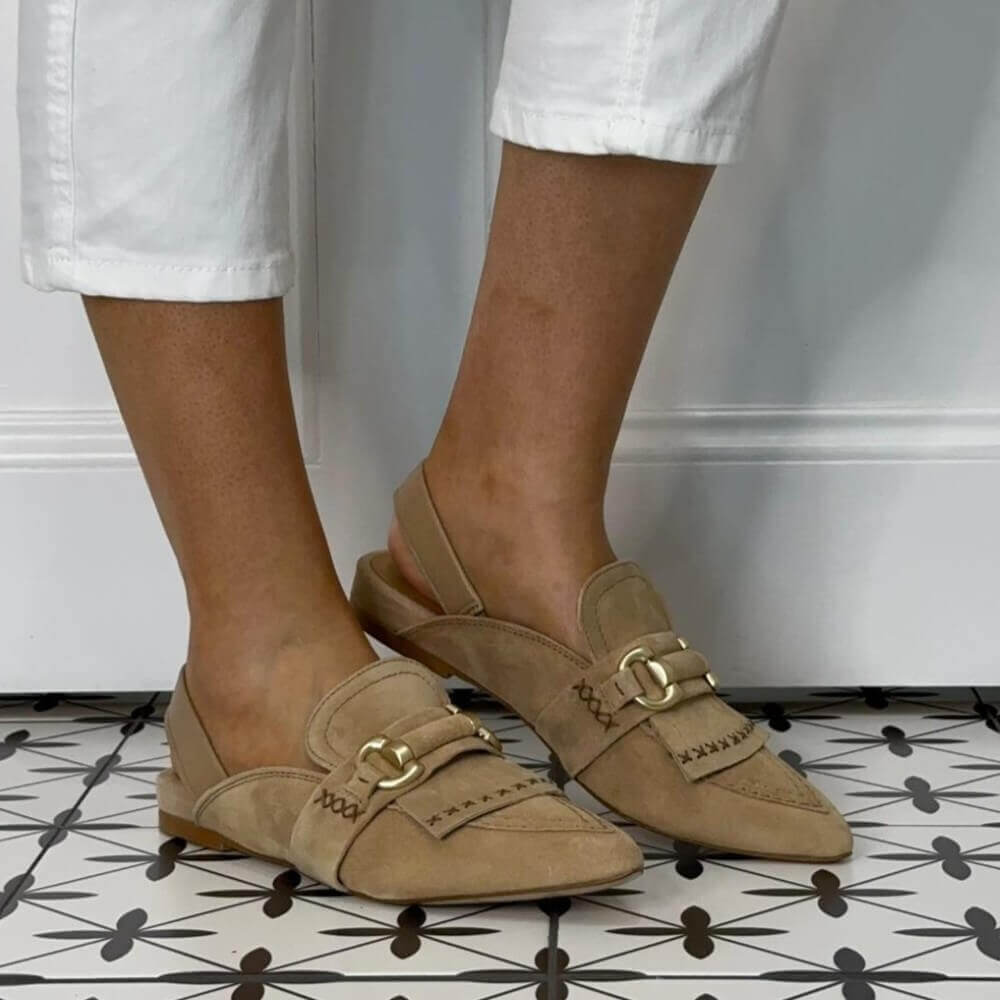 MJUS Beige loafers with gold buckles worn by a person on a patterned floor.
