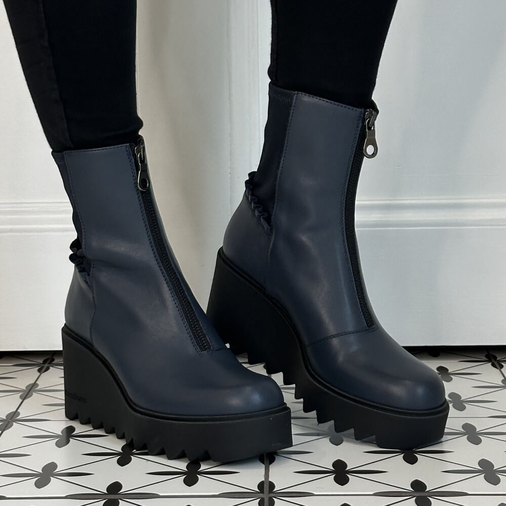 A pair of Marco Moreo dark navy blue leather ankle boots with chunky black platform wedge soles and front zippers, shown on a person wearing black leggings.