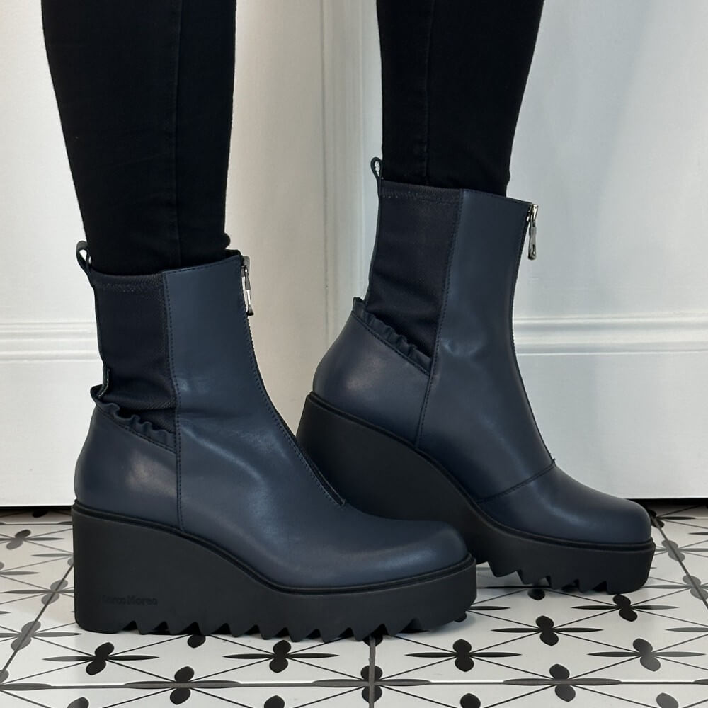A pair of Marco Moreo dark navy blue leather ankle boots with chunky black platform wedge soles and front zippers, shown on a person wearing black leggings.