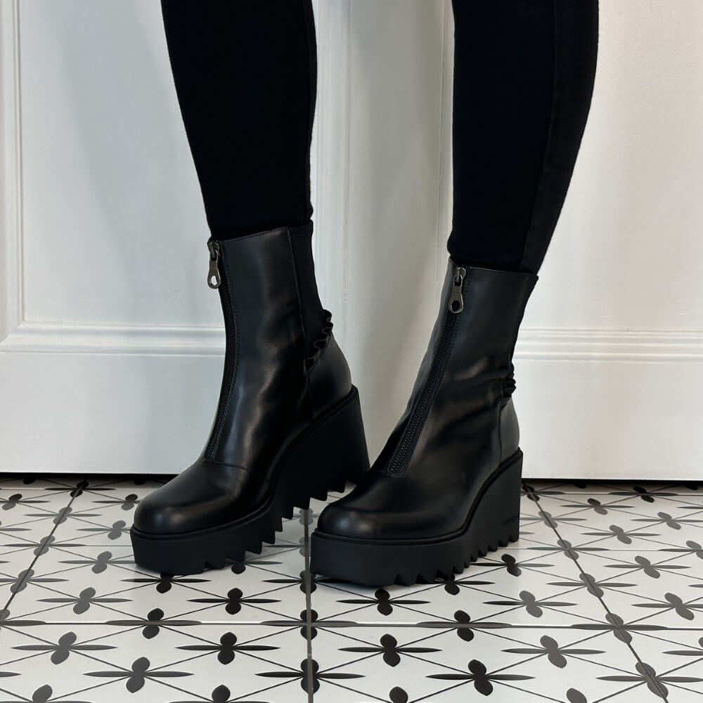 Marco Moreo Black platform ankle boots with front zippers, worn with black leggings on a black and white patterned tile floor in front of a white wall.