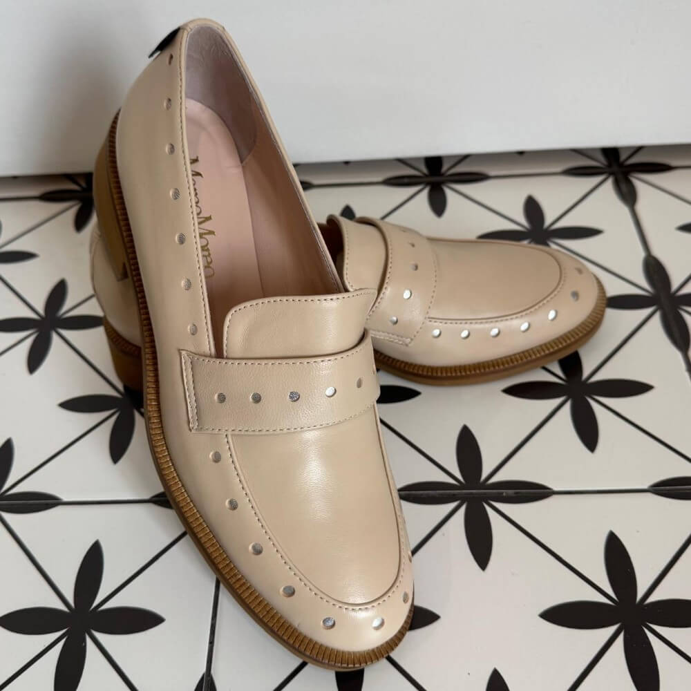 Pair of Marco Moreo beige loafers with brown soles on a white and black patterned floor. Maura X705