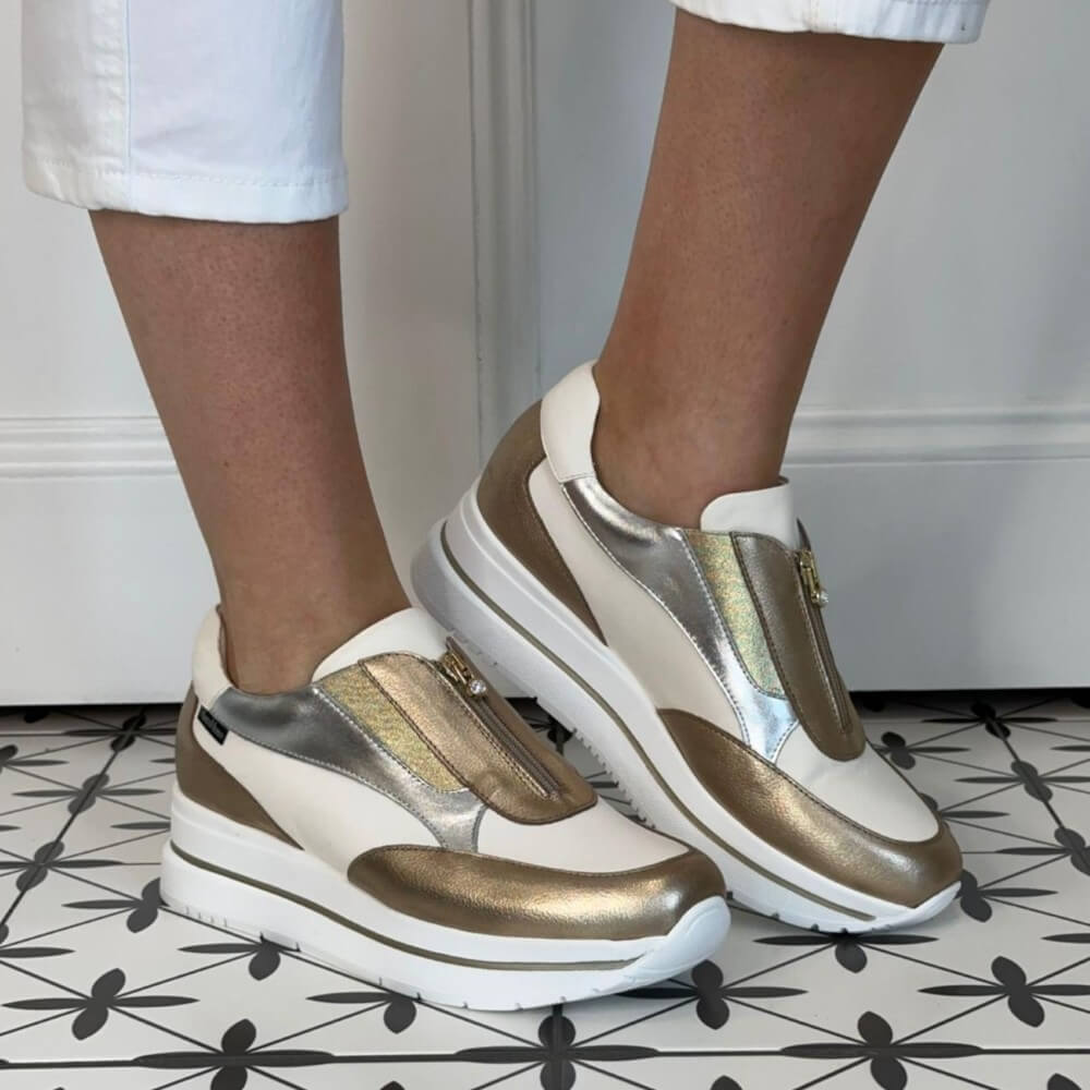 Marco Moreo White and gold sneakers worn by a person on a patterned floor.