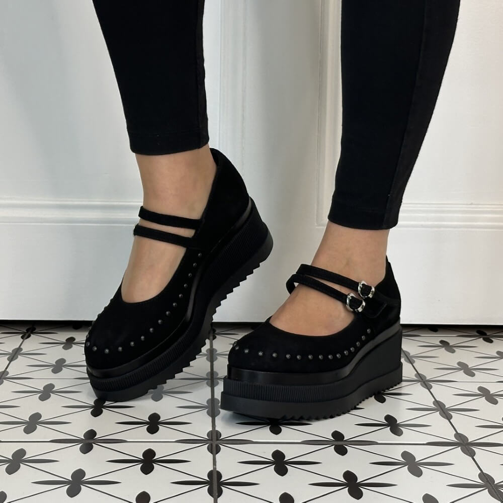 Marco Moreo Black platform Mary Jane shoes with double straps and silver buckles, shown on a model wearing black leggings against a white panelled wall and patterned tile floor.