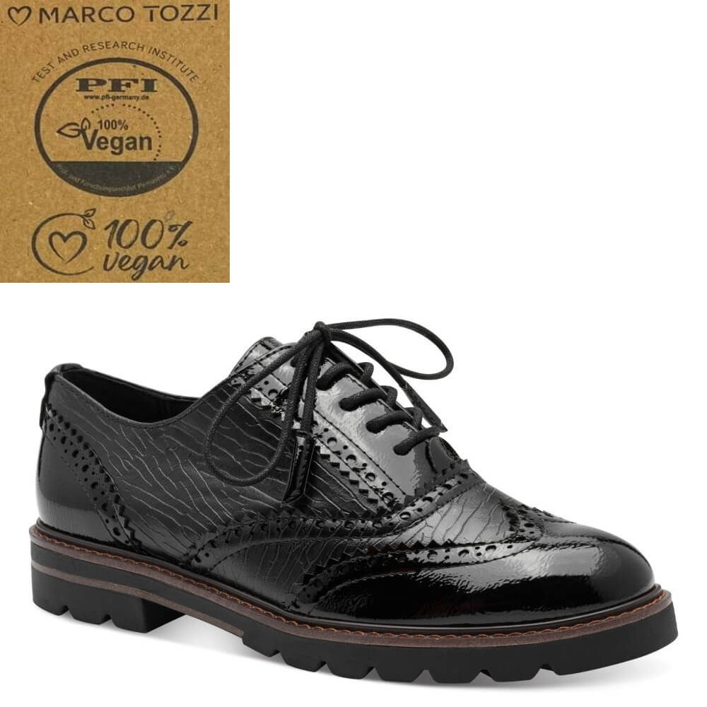 A black glossy vegan leather oxford-style shoe with brogue detailing and black laces, shown on a white background. A brown cardboard badge in the top-left corner reads 'MARCO TOZZI' and 'PFI 100% Vegan'.