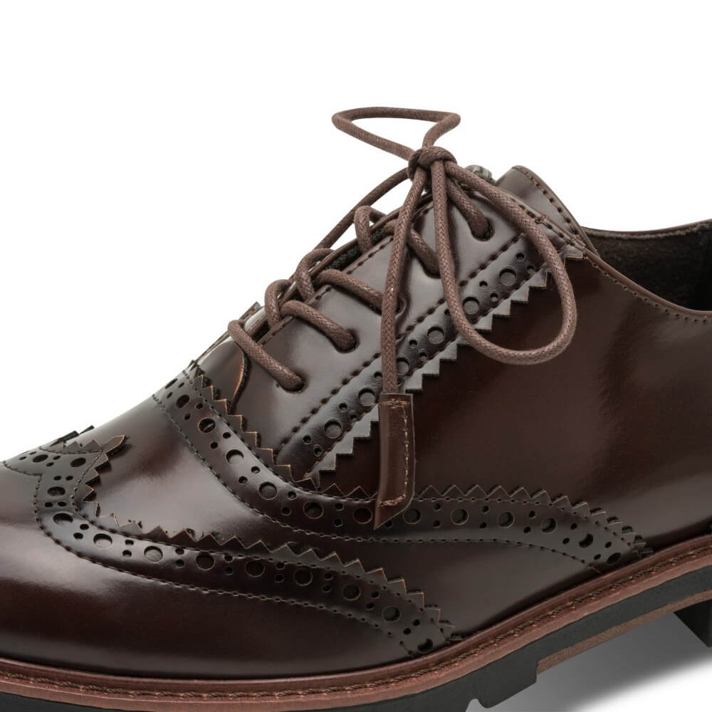 A close-up of a dark brown vegan wingtip oxford shoe with decorative brogue perforations and matching brown laces, shown on a white background.