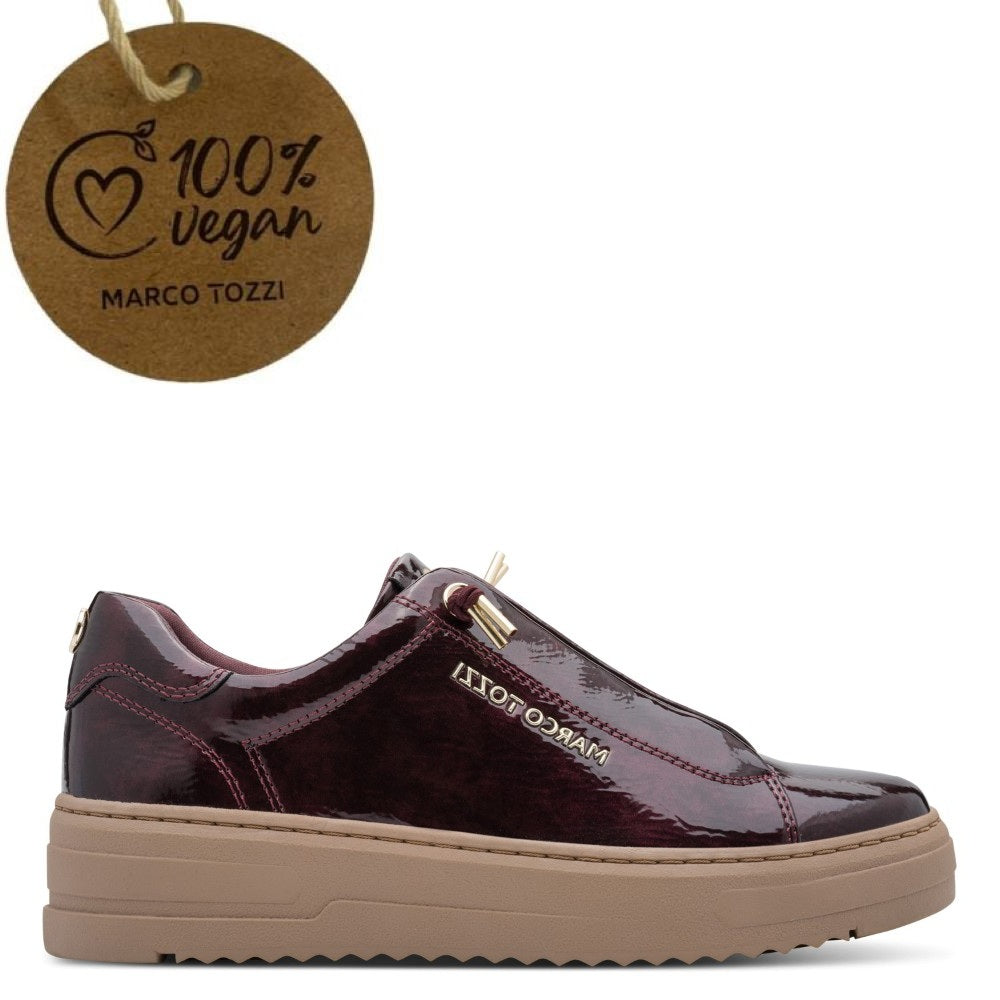 A low-top slip-on shoe in glossy burgundy patent vegan with a tan rubber sole, shown on a white background with a hanging paper tag that reads '100% vegan MARCO TOZZI'.