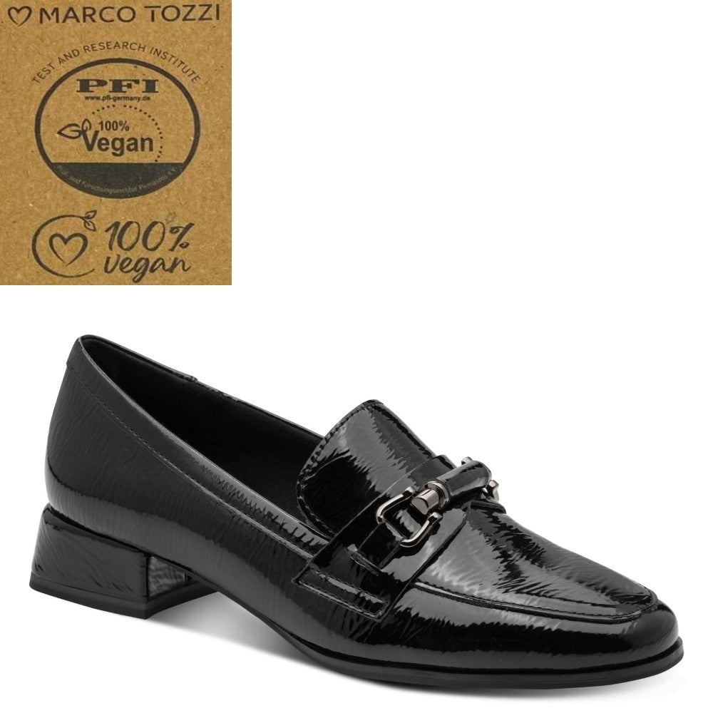 A Marco Tozzi black patent Vegan loafer by Marco Tozzi, featuring a low block heel and a decorative buckle strap across the vamp. The shoe is displayed on a clean white background with a brown cardboard certification badge in the top-left corner.